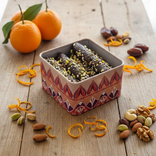 Decorative tin with dried fruits and nuts on a wooden surface with oranges and orange peels.